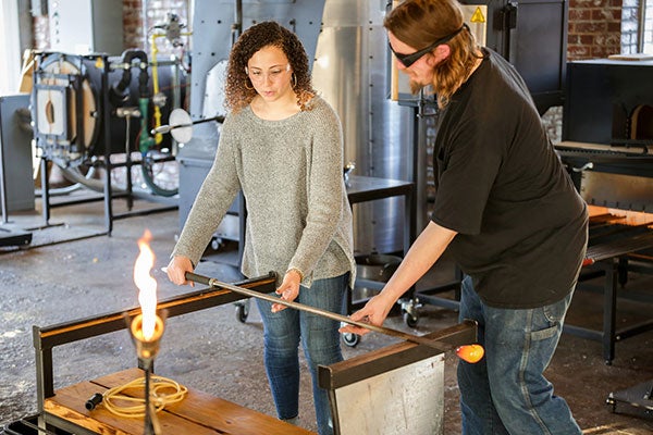 A teacher helps a student with glass blowing